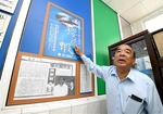 ２００１年４月に東港で行われたサクラエビの地元需要拡大イベントのポスターを指さす陳春朝さん＝２月下旬、台湾・長治郷の朝海生物科技社