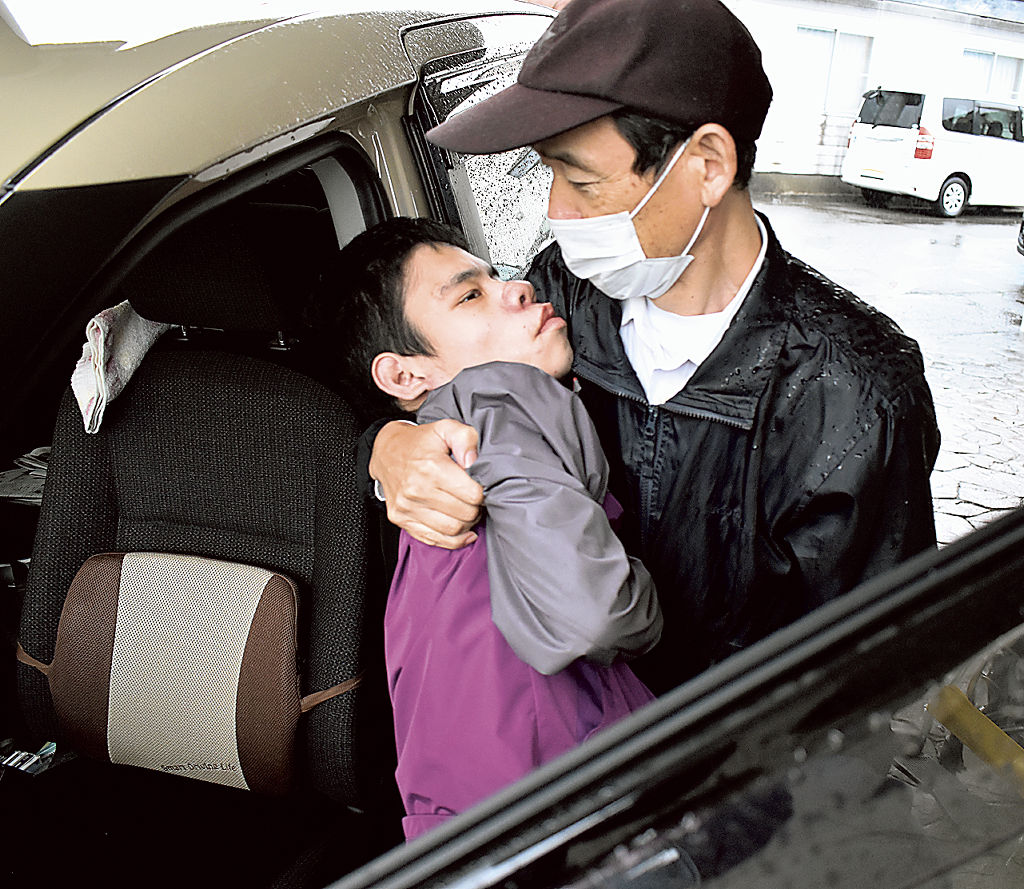 息子隼さんを５８歳の体で抱え、車に運び込む渡辺裕之さん＝静岡市清水区、５月下旬