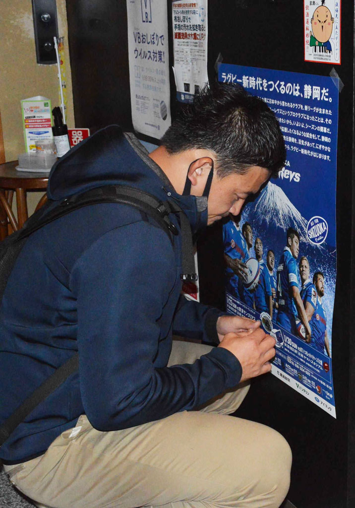 飲食店にポスターを貼る五郎丸歩さん＝１２月初旬、浜松市内