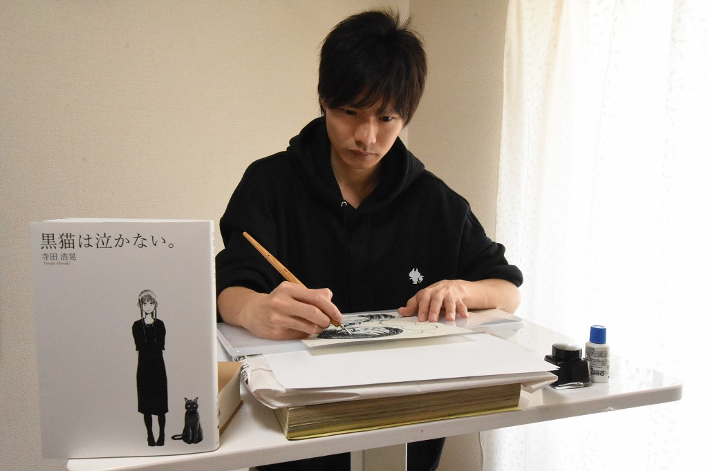 自身初の書籍を出版する漫画家の寺田浩晃さん。長時間座ることができず、立ったまま執筆作業に励んでいる＝磐田市