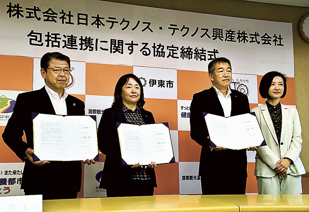 協定書を掲げる小野市長（左）と塩川社長（中央左）ら＝伊東市役所
