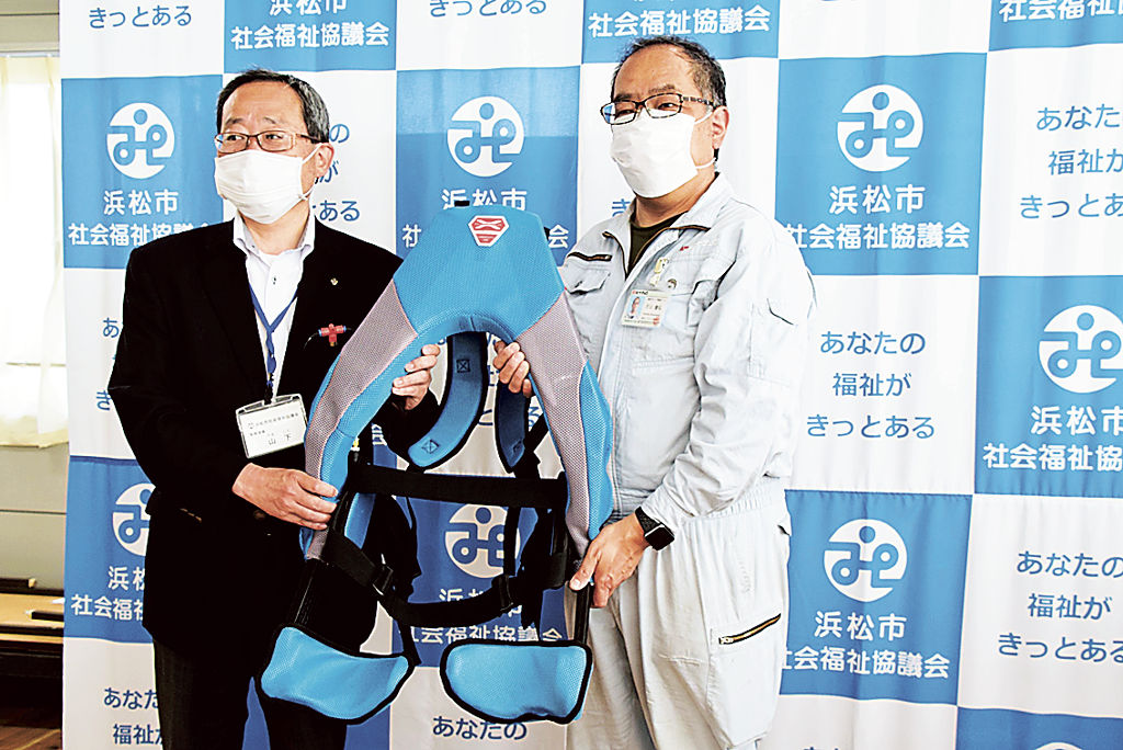 浜松市社会福祉協議会の山下常務理事（左）にパワードスーツを手渡す片山さん＝同市中区