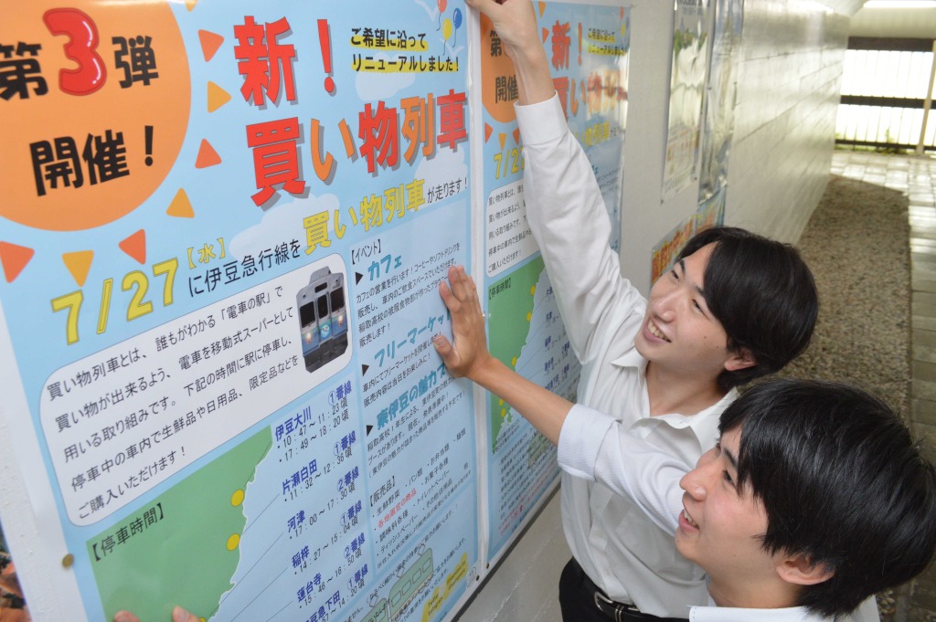 駅にポスターを掲示する太田港士さん（左）ら＝７月上旬、東伊豆町の片瀬白田駅