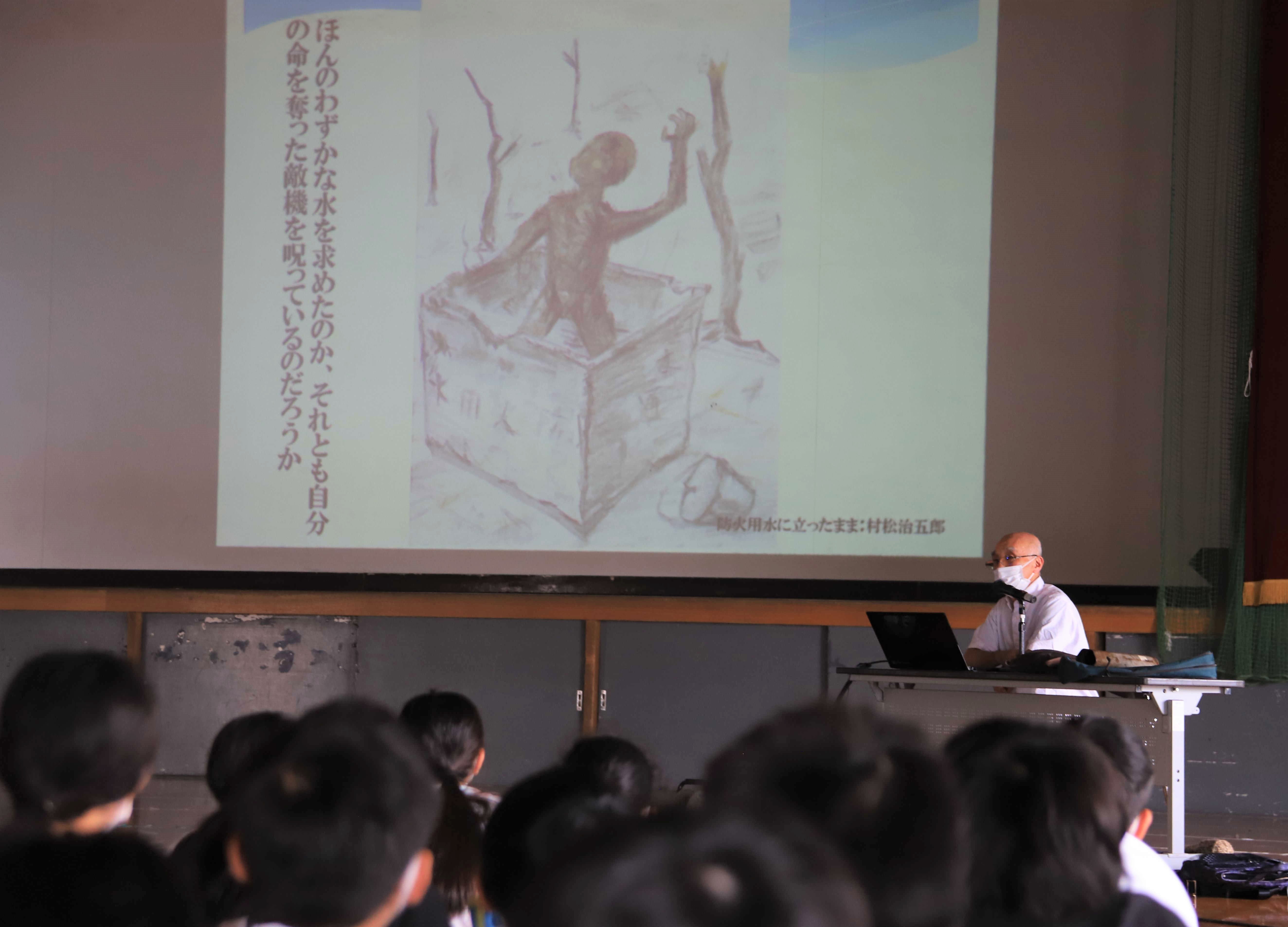 静岡空襲の経験者が描いた絵を児童に見せる田中明充さん＝６月中旬、静岡市葵区の竜南小