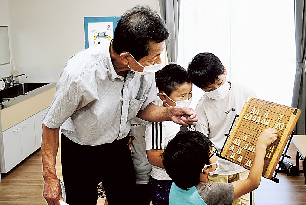 池田会長（左）の指導を受けながら、将棋の基礎を学ぶ児童＝吉田町内