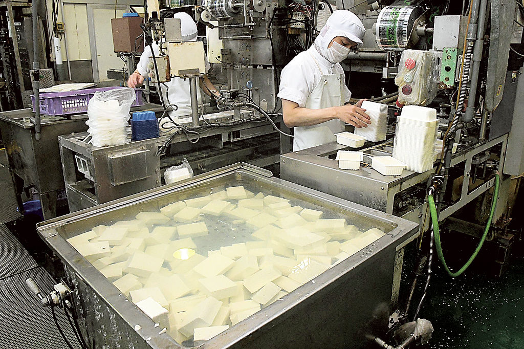 豆腐をパックに詰める従業員。原料の大豆の仕入れ値は高止まりしている＝静岡市清水区