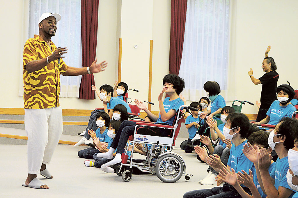 マーティンさん（左）の歌に合わせて手拍子をする学園生＝掛川市上垂木のねむの木学園