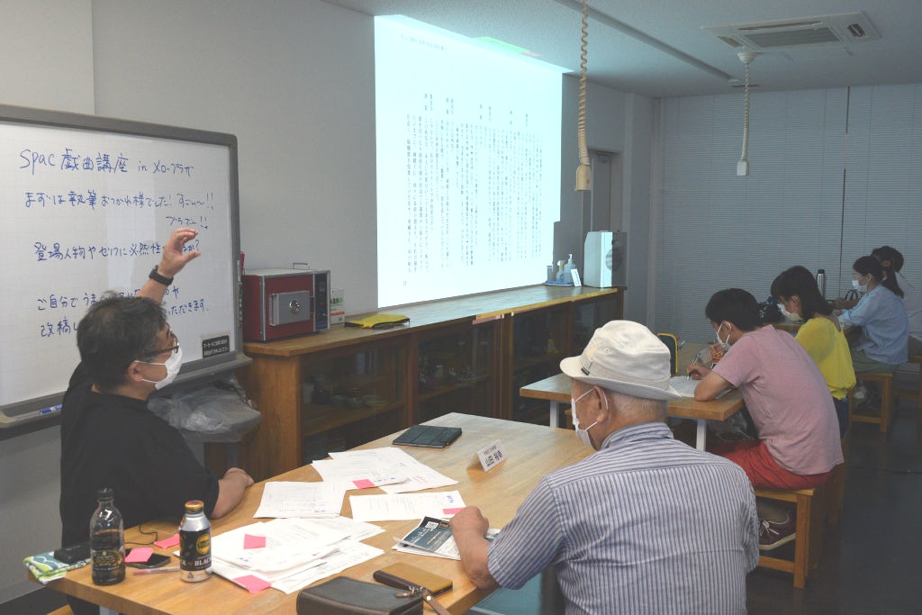 講師の山田さん（左）の助言を聞く受講者。戯曲作りを通じて演劇を学ぶ＝袋井市のメロープラザ