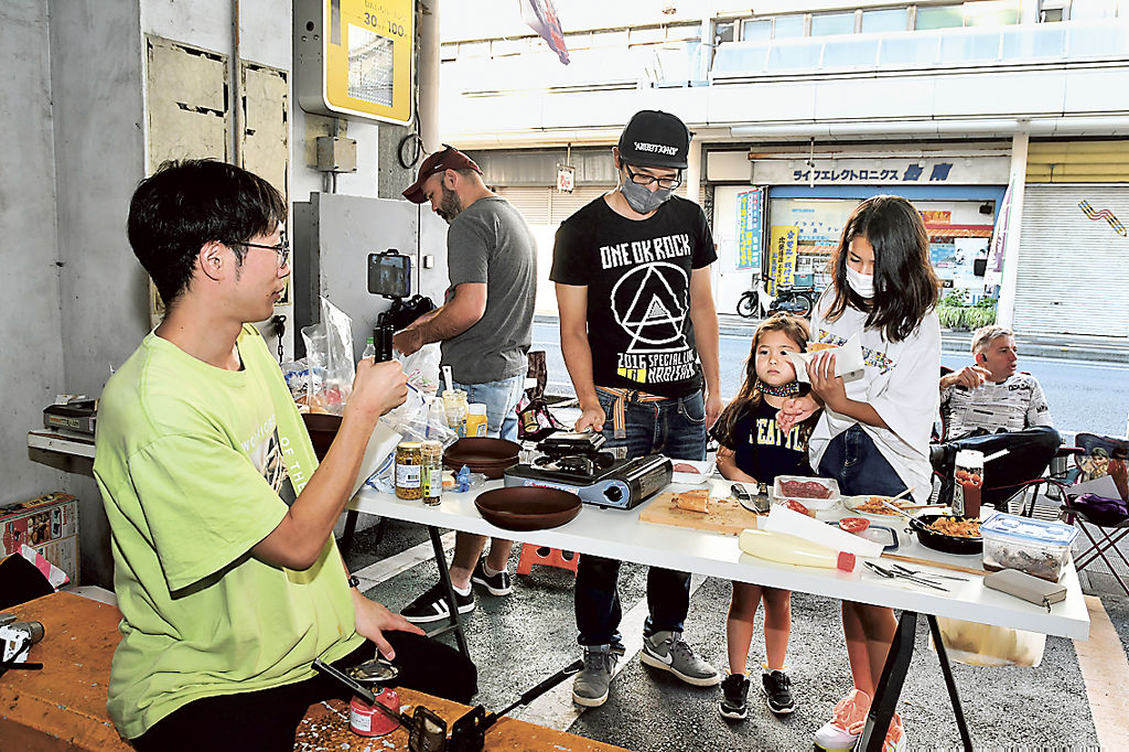 ホットサンドを食べながら出自を話す住民を撮影するＲｕｉさん（左）＝富士市の吉原商店街