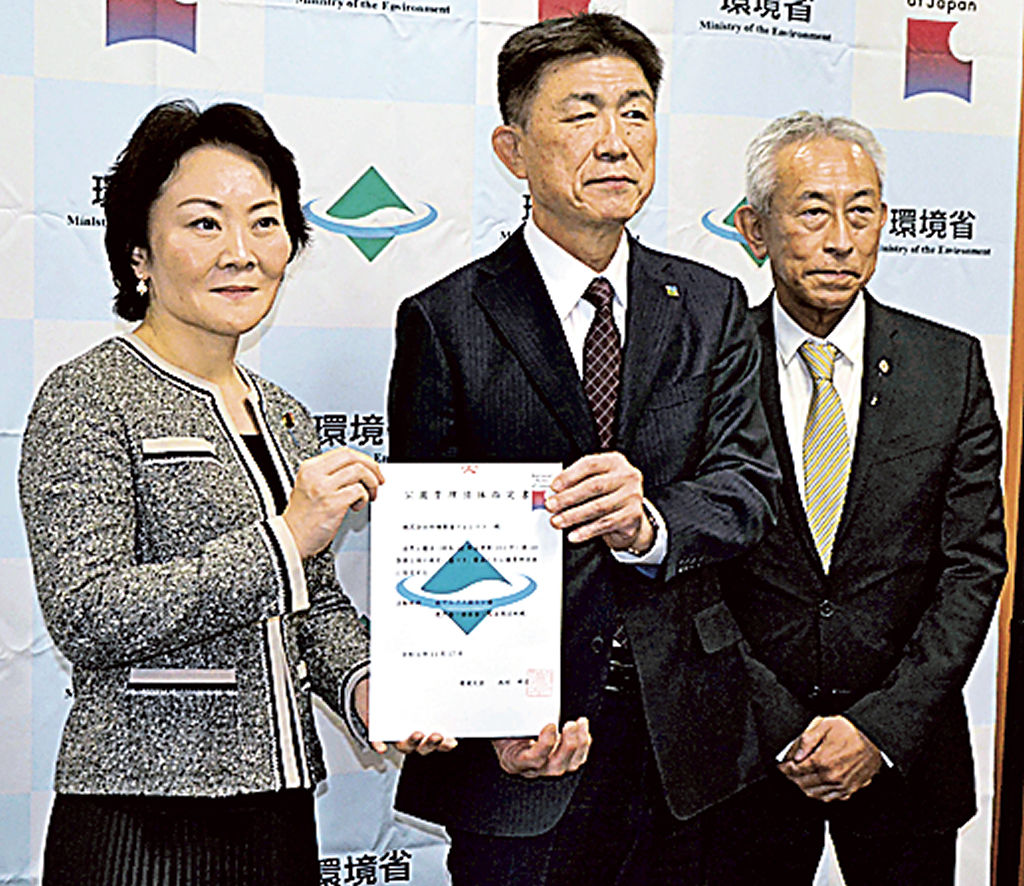 山田美樹副大臣（左）から指定書を受け取る亀山寿夫社長（中央）＝１７日午後、環境省