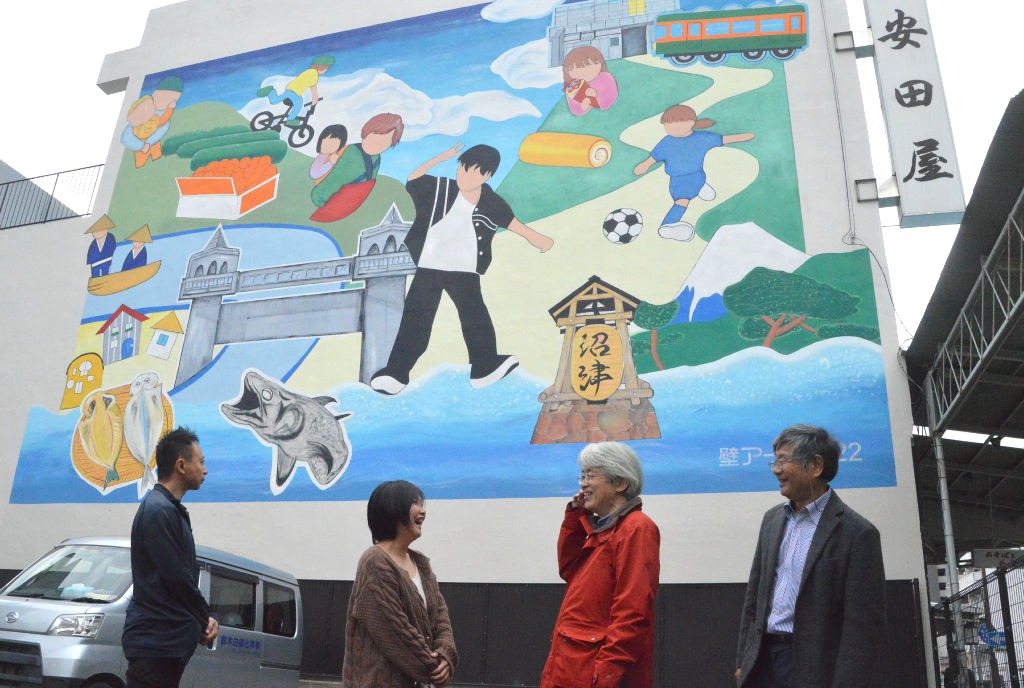 戸塚さん（左から２人目）の原画を基にそば店の壁に描かれた壁画＝沼津市本町