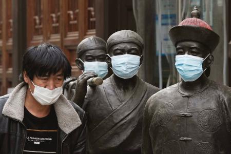 マスクを着けた銅像の前を通る人＝１２日、北京（共同）