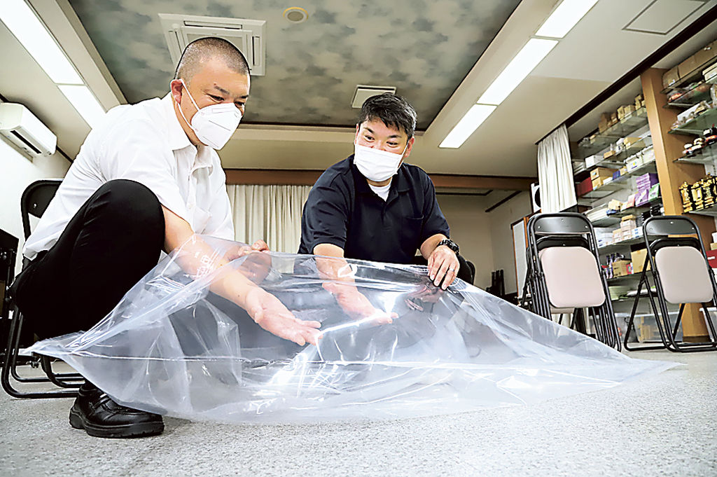 遺体を収める納体袋を手にする葬儀社の関係者＝９月、松崎町