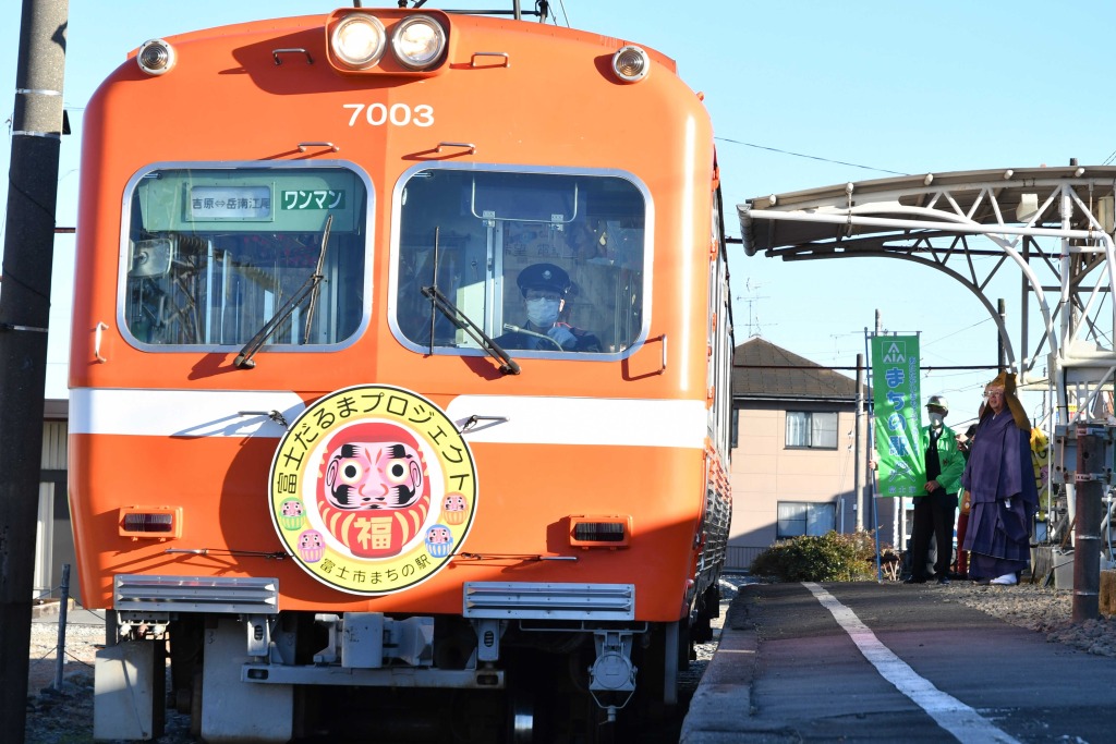 だるまが描かれたヘッドマークを付けて出発する電車＝富士市の岳南江尾駅