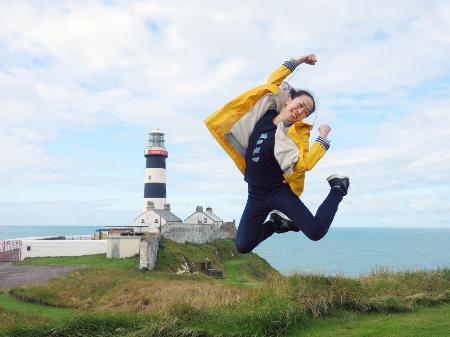 アイルランドにある灯台の前でジャンプする不動まゆうさん＝２０１９年（本人提供）