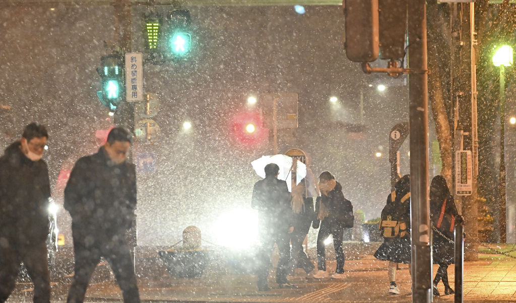 強風で小雪が舞う中、家路を急ぐ人たち＝２４日午後８時４５分、浜松市中区（浜松総局・二神亨）