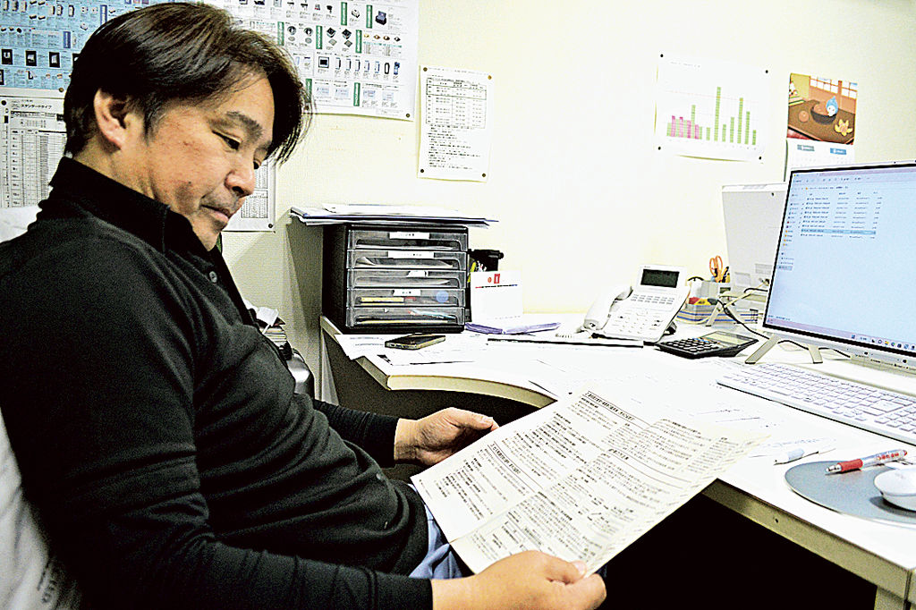 インボイス制度に関する資料を眺める角田充博代表取締役。登録番号を管理するシステムを導入した＝２月中旬、静岡市駿河区