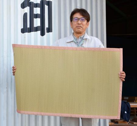 乳児用の寝ござを手にする、畳表の卸問屋を営む北川昌義さん＝１５日、熊本県八代市