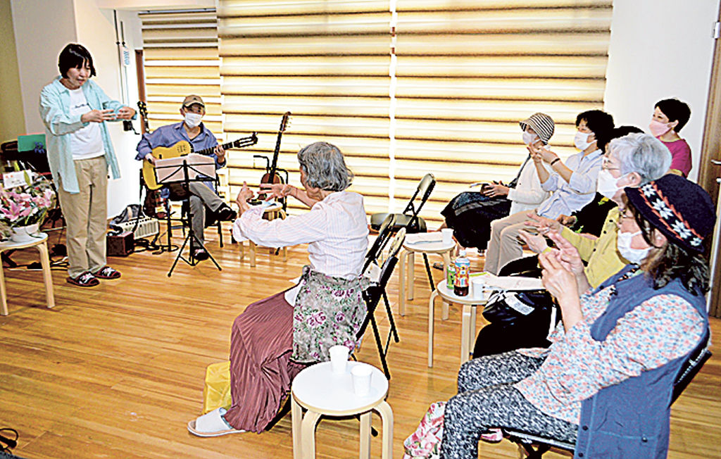 松野代表（左）と一緒に歌いながら手話に挑戦する高齢者ら＝熱海市和田浜南町