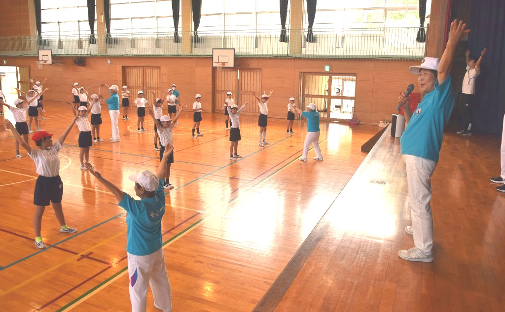 指導士（右）と一緒にラジオ体操をする児童たち＝５月下旬、焼津市栄町の焼津東小