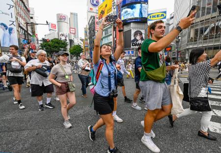スマートフォンで撮影しながら東京・渋谷のスクランブル交差点を横断する米国からの観光客＝１０日午後
