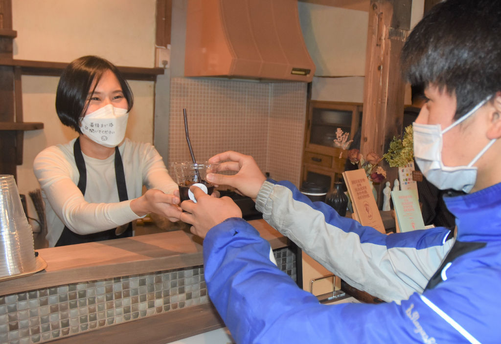 商品を手渡す奥村安莉沙さん（左）。マスクには「最後まで聞いてください」とのメッセージが書かれていた＝１月下旬、宇都宮市