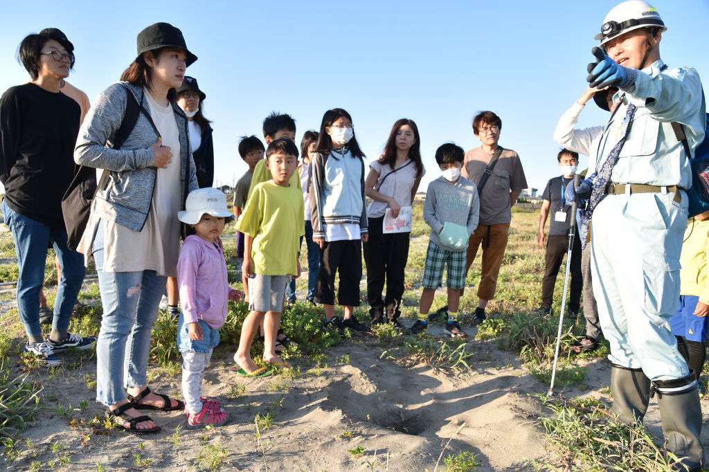 曽根さん（右）の説明を聞きながら、アカウミガメの保護監視活動について学ぶ参加者＝御前崎市