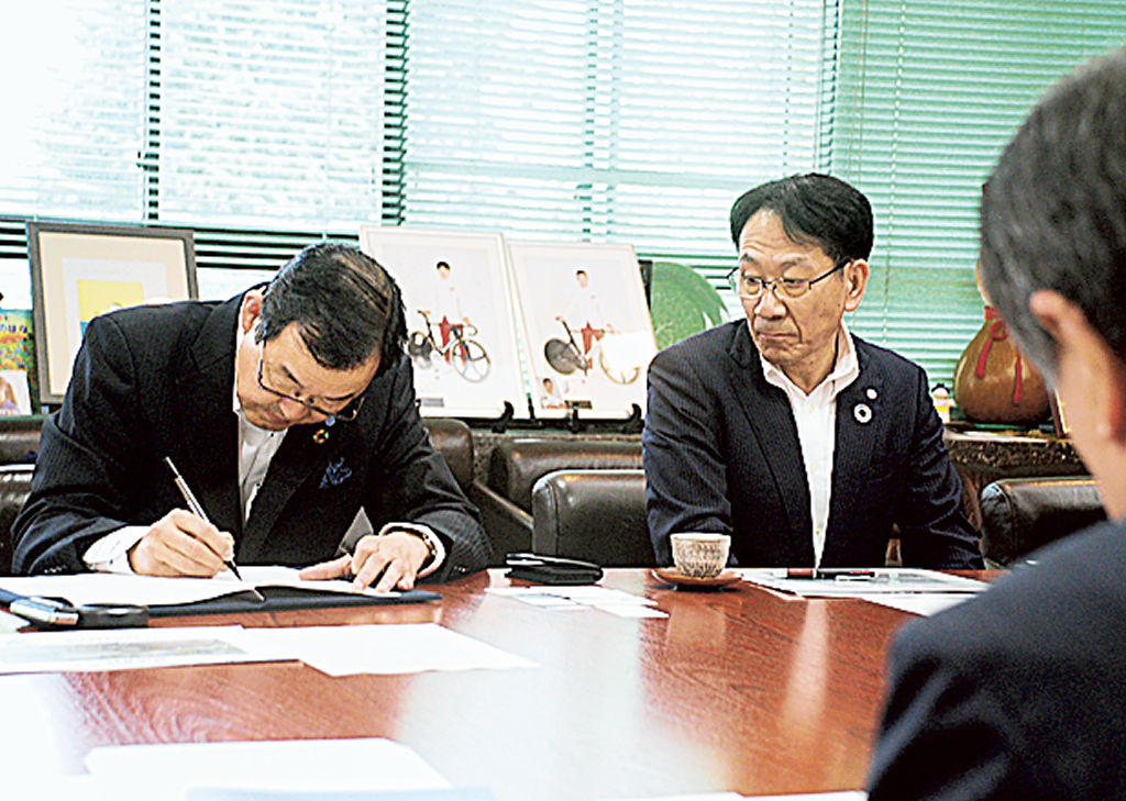 協定書にサインする彦坂社長（左）＝三島市役所
