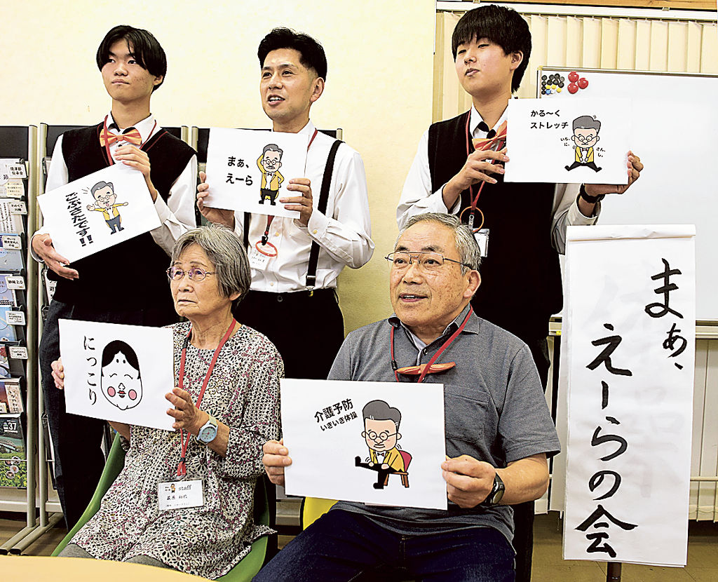マギー司郎さんのイラストを入れたオリジナルＬＩＮＥスタンプのデザイン画を持つマギー塁さん（後列中央）ら「まあ、えーらの会」メンバー＝焼津市本町