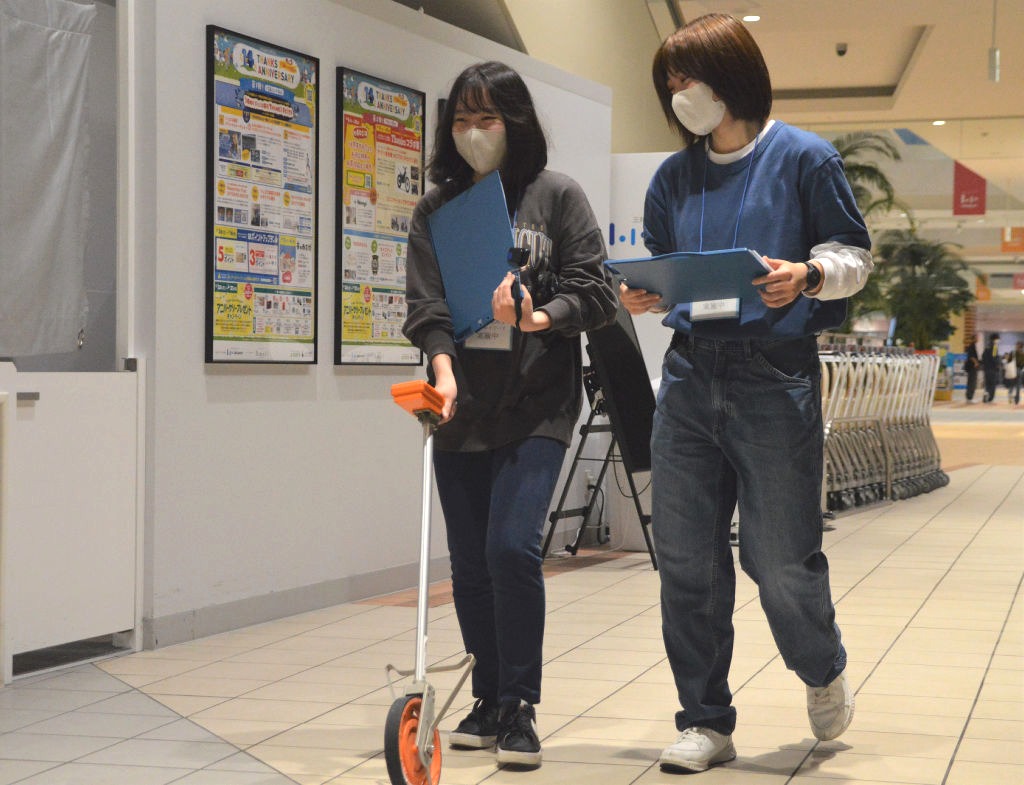 距離計測器を手に館内を歩き回る静岡産業大の学生たち＝磐田市高見丘のららぽーと磐田