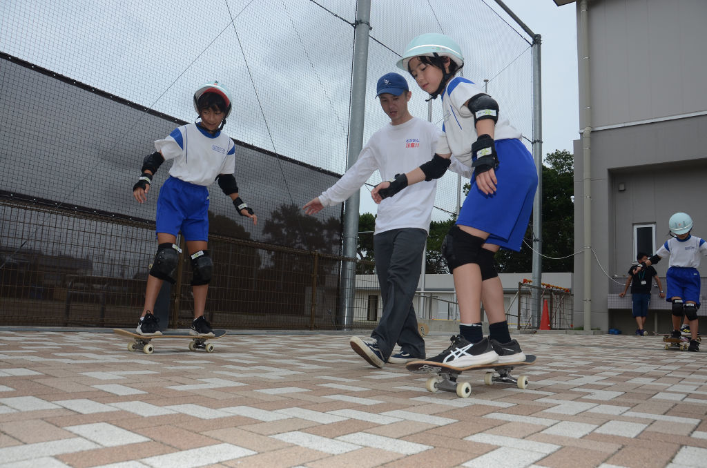 近藤さん（中央）の指導でスケートボードを体験する児童＝浜松市中区の船越小