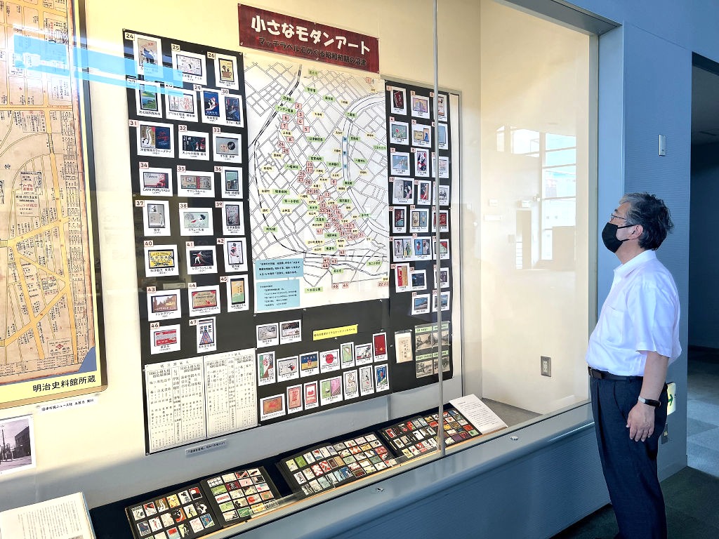 昭和初期のマッチ箱ラベルに描かれた店舗の場所を調べた山本さん＝沼津市立図書館