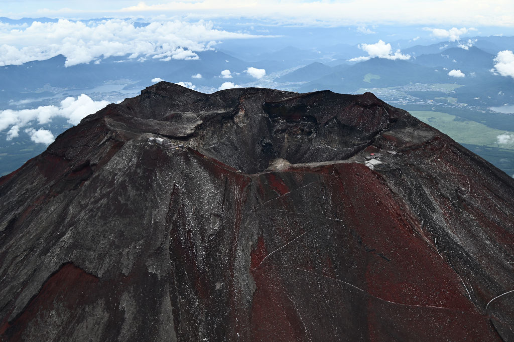 赤い山肌を見せる夏の富士山。山頂付近はうっすらと雪に覆われた＝１日午前（静岡新聞社ヘリ「ジェリコ１号」から、写真部・久保田竜平）