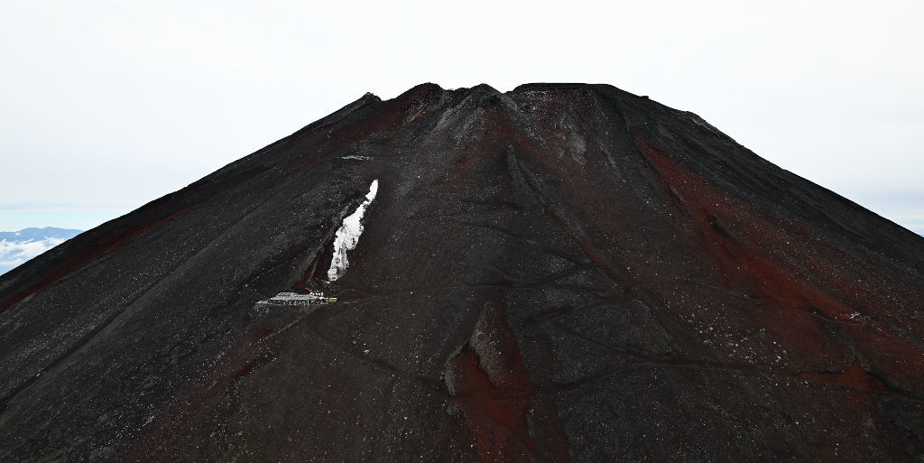 赤い山肌を見せる夏の富士山。手前左は臨時支局を開設した万年雪山荘＝１日午前（静岡新聞社ヘリ「ジェリコ１号」から、写真部・久保田竜平）