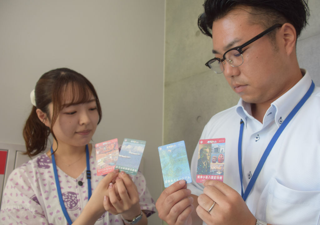 市内施設に置かれている４枚のカードを持つ企画した職員＝焼津市役所