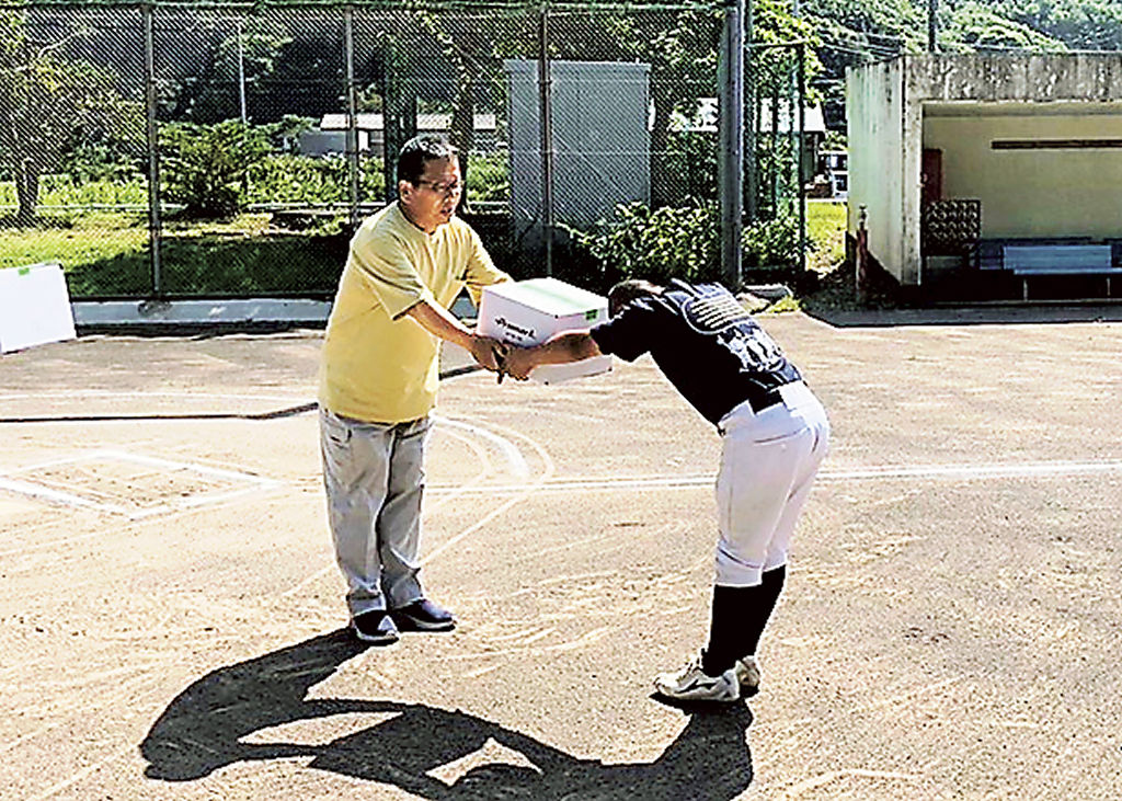 代表児童にボールを手渡す佐藤社長（左）＝松崎町の町営総合グラウンド