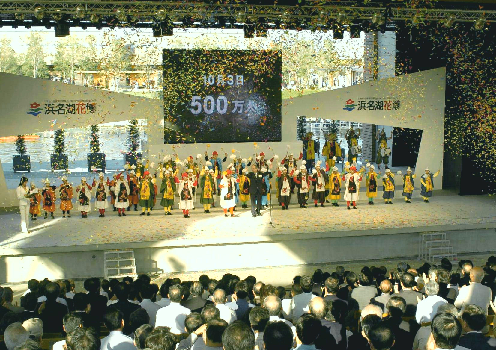 ５００万人と映し出された大型スクリーンの前で舞踊のパフォーマンスを見せる小中学生ら＝浜松市村櫛町の花博会場・水辺の劇場