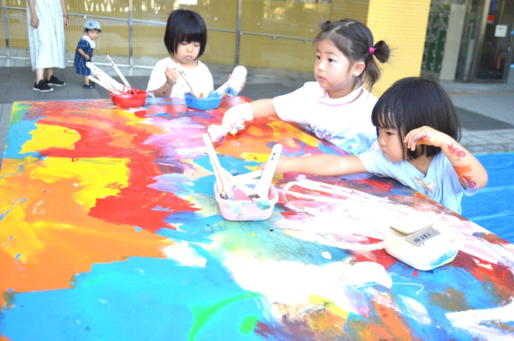 テーブルにペイントする子どもたち＝２日午前、長泉町のＪＲ下土狩駅前のコミュニティながいずみ北口広場