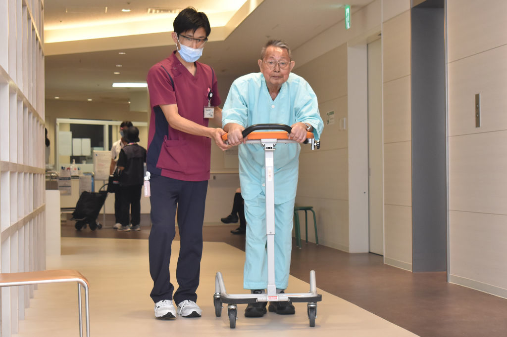 集大成となる写真展の成功に向け、入院中の病院でリハビリに励む岩本雅志さん（右）＝９月上旬、掛川市内