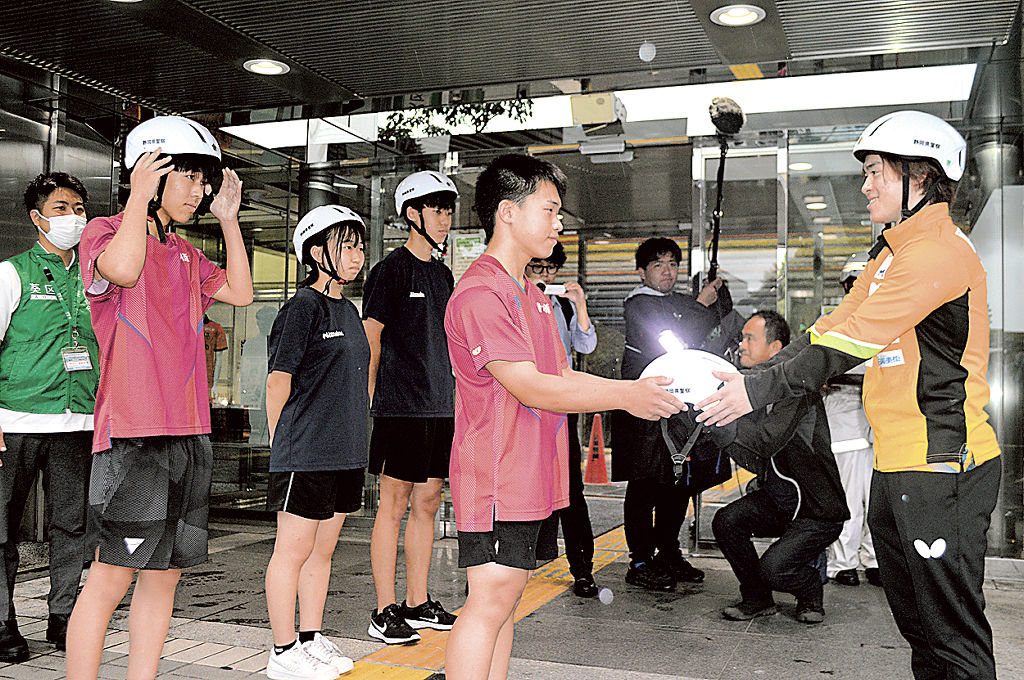 森薗監督兼選手（右）からヘルメットを受け取る生徒＝静岡市役所静岡庁舎前