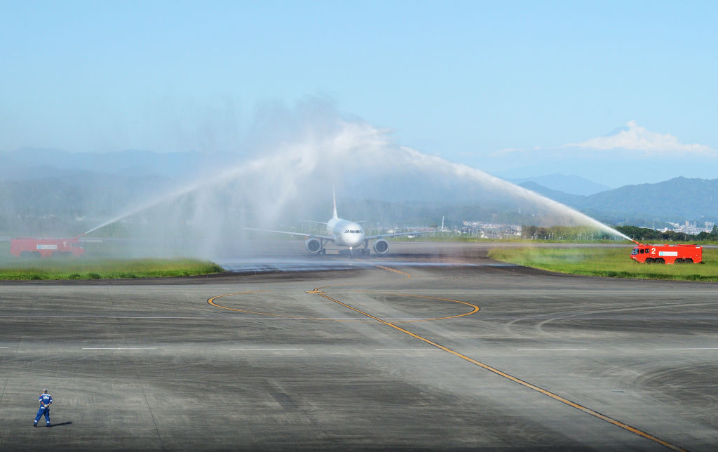 富士山を背に放水アーチによるおもてなしを受ける機体＝２４日午後、静岡空港
