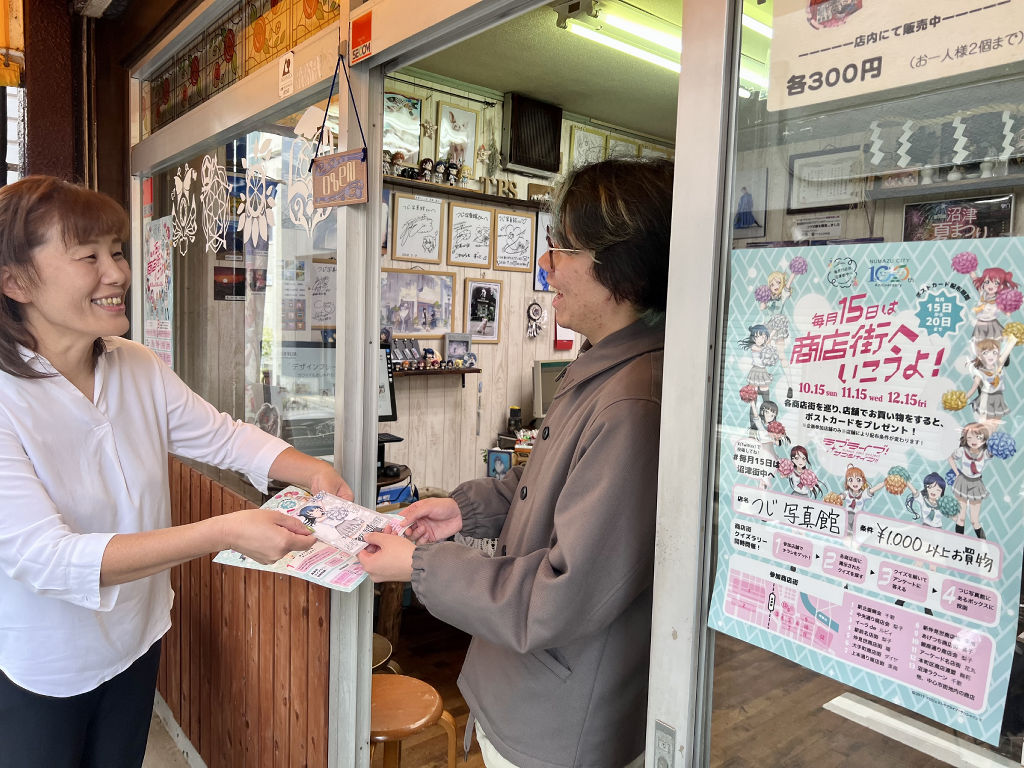 ポストカードを小田さん（右）に手渡した峯さん（左）＝沼津市のつじ写真館