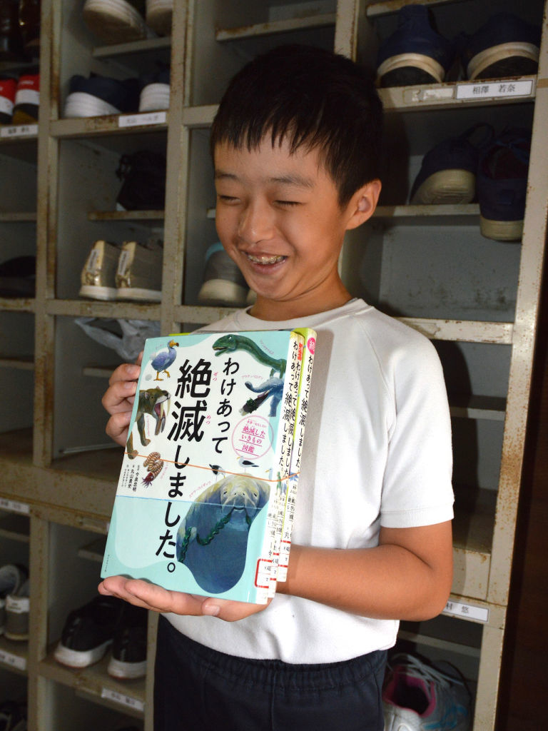 海を越えて届いた図書館の本を手に笑顔の中石陸斗さん。「たくさん読みたい」と話す＝１０月上旬、熱海市立初島小・中