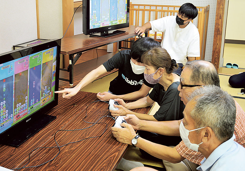 パズルゲームを体験する参加者。真剣な表情で画面を見つめ機械を指で動かしている＝９月下旬、磐田市の富岡交流センター