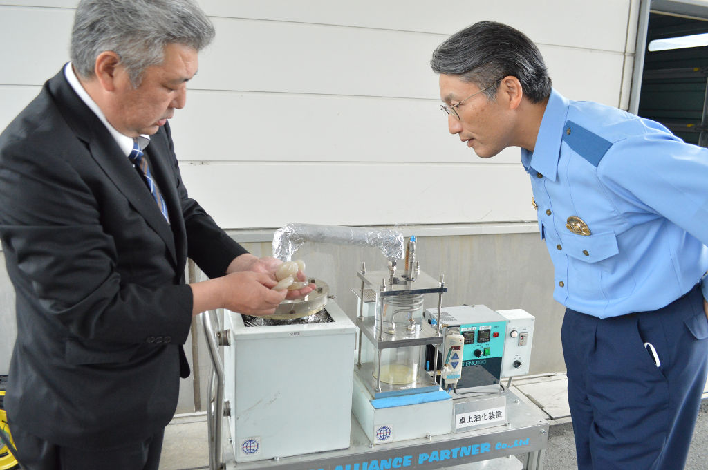 リサイクル油ができるまでの課程を説明する赤松社長（左）＝１０月上旬、裾野署