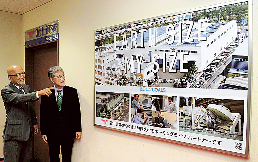教室の命名権を取得して設置したボードを紹介する石沢社長（左）＝浜松市中区の静大浜松キャンパス