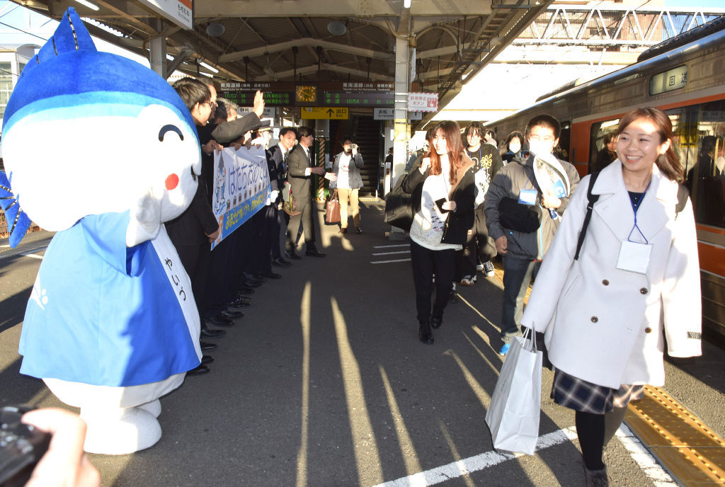「やいちゃん」（左）やオリジナルの横断幕で出迎えられる新成人たち＝焼津市のＪＲ焼津駅