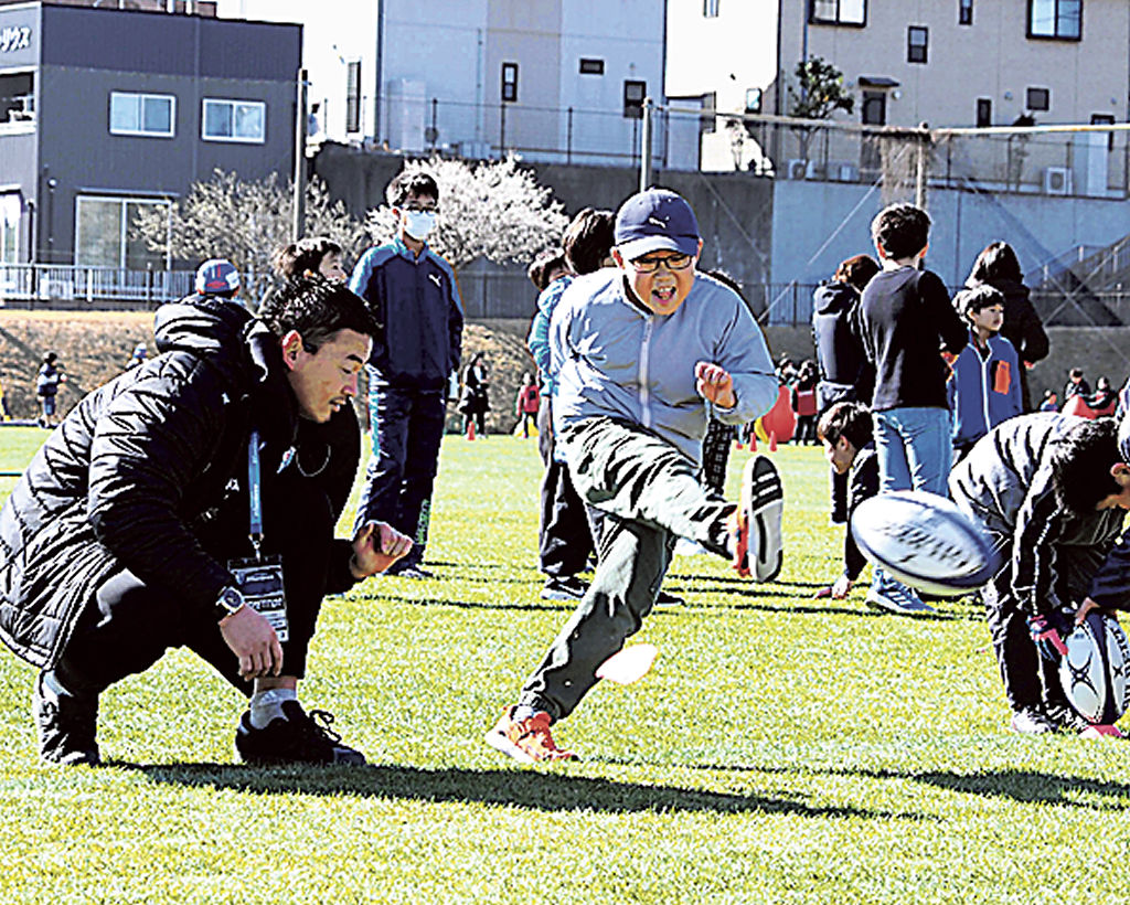 五郎丸さん（左）の手ほどきでラグビーボールのキックを体験する子ども＝磐田市の安久路公園