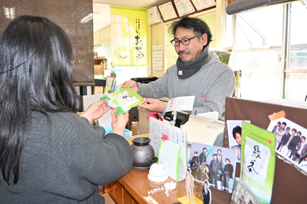 緑茶ティーバッグを手にファンと交流する堀井聡理事（右）。店には訪れたファンが置いたグッズが並ぶ＝１月下旬、掛川市五明の五明茶業組合