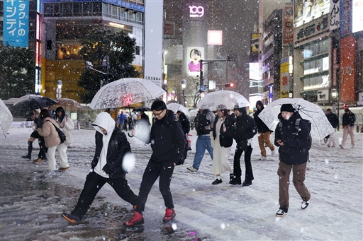 雪が降る中、東京・渋谷のスクランブル交差点を歩く人たち＝５日夜